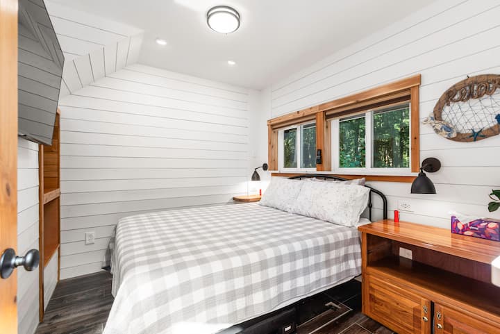 חדר שינה בקומה הראשית עם מיטת קווין סייז, וילונות האפלה וטלוויזיה. 