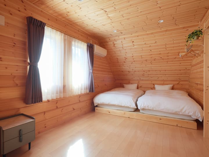 明るい木製の壁と白い布団のベッドが置かれたベットルームです。