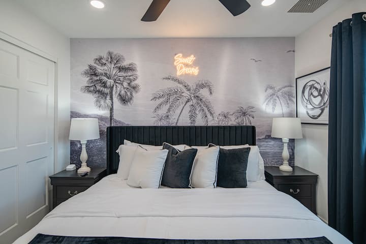Coastal Dreams – Een rustige ontsnapping met moderne zwarte meubels, fris wit beddengoed en een luchtige muur met palmbomen. 