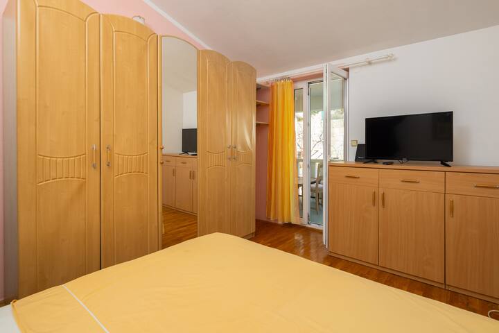 Quarto com cama de casal, guarda-roupa, TV de tela plana e varanda