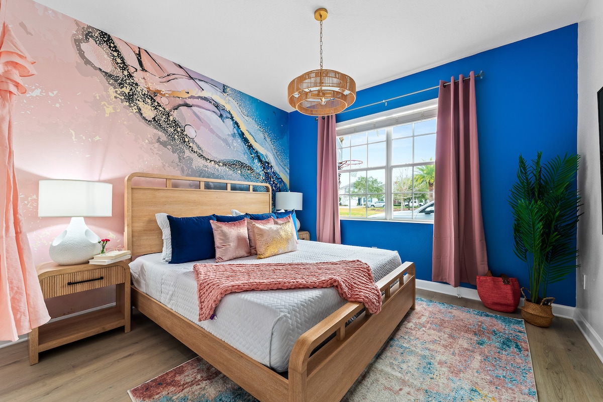 Ярко и стилно място за отдих! Тази мечтана спалня разполага със смели сини стени, меки розови акценти и зашеметяващ артистичен стенопис. Отпуснете се в уютно двойно легло king size и се събудете с красива естествена светлина. Идеално за шикозен и освежаващ престой! #DreamEscape