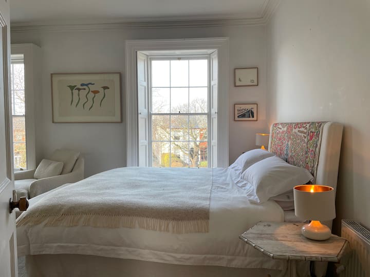 Cama super king size con lujosas almohadas y edredón. Dos ventanas con vistas desde el último piso, con vistas al vecindario, las copas de los árboles y el cielo
