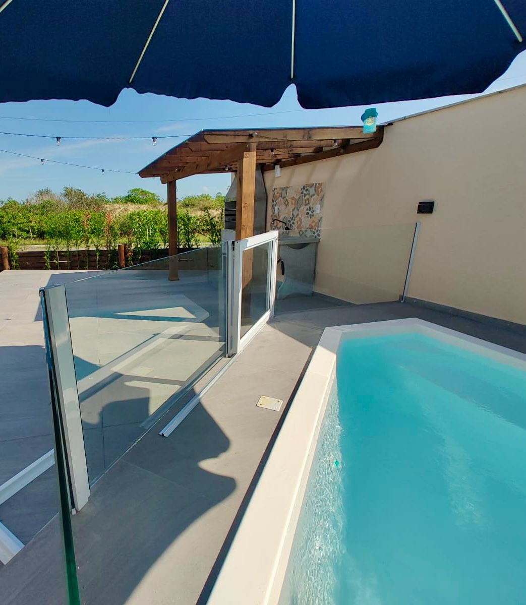 A well-maintained outdoor area features a private jacuzzi surrounded by sleek glass fencing. A shaded area with wooden beams offers a cozy spot for relaxation. The style of the space incorporates modern design elements, enhancing the tranquil ambiance.