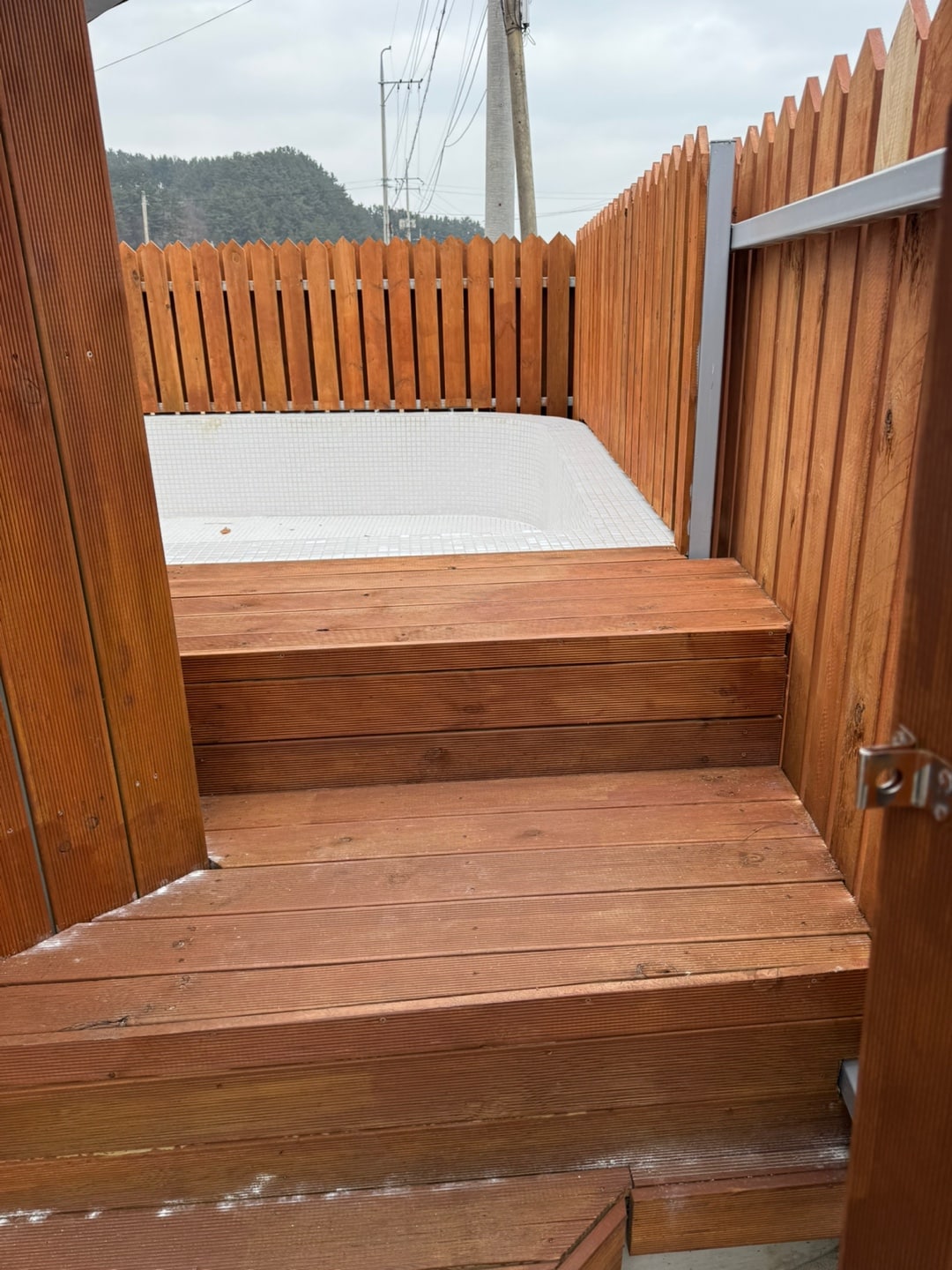 A wooden staircase leads up from a fenced area, showcasing a clean and spacious deck area atop. Natural wood tones are emphasized by a slightly cloudy sky in the background, adding to the outdoor ambiance.