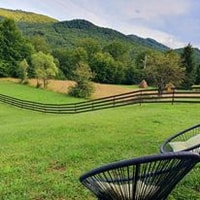 A spacious outdoor area is highlighted by lush green grass and rolling hills in the background. Fencing surrounds the property, adding structure to the scenic view. Two comfortable seating chairs are positioned to enjoy the serene landscape.