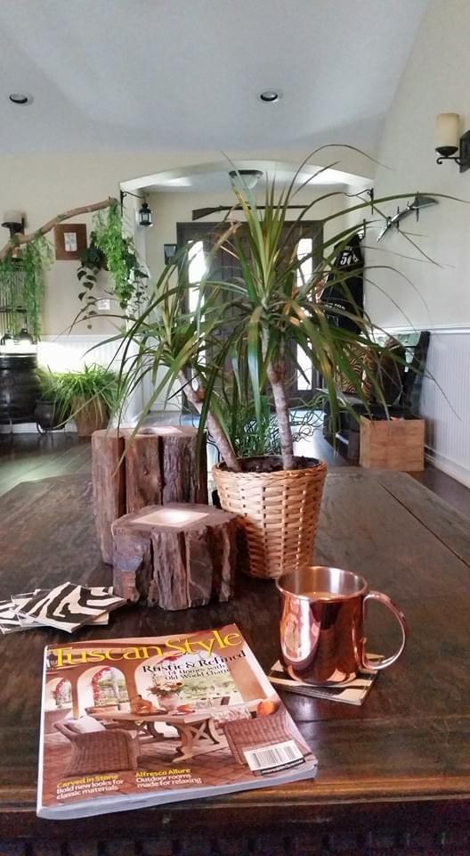 A spacious table is adorned with a copper mug and a magazine on a coaster. A woven basket containing a potted plant adds a touch of greenery. Natural wood elements complement the decor, with soft lighting enhancing the inviting atmosphere of the room.