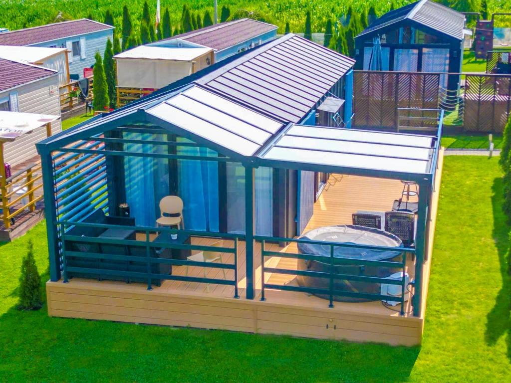 The outdoor space features a spacious terrace with clear roofing and elegant railings. A private jacuzzi is accessible, accompanied by comfortable seating. Lush greenery surrounds the area, enhancing the cozy atmosphere of the retreat. Nearby, additional cabins are also visible.