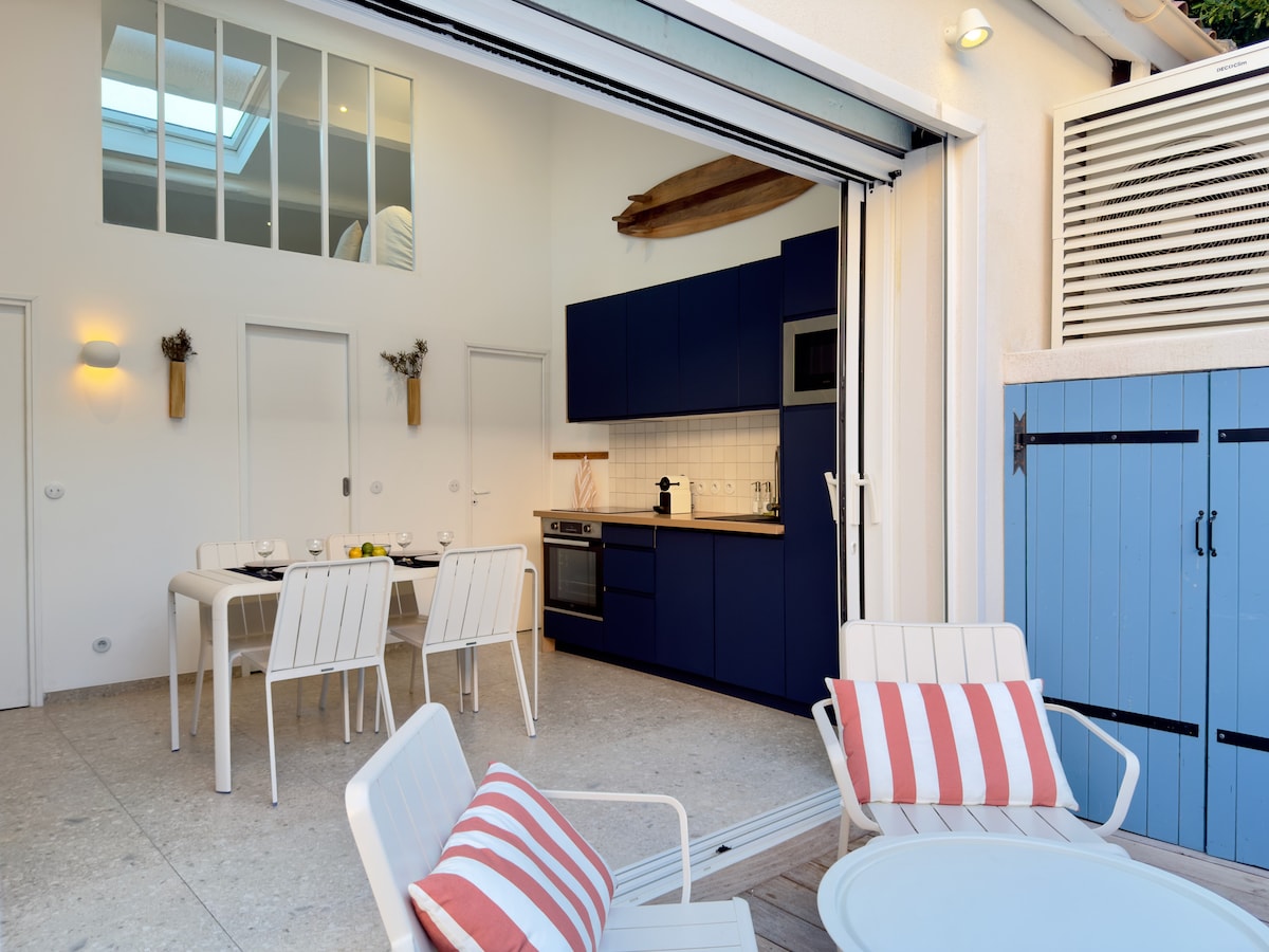The open-concept kitchen and dining area features modern blue cabinetry and stainless steel appliances. A spacious dining table is arranged for six, complemented by light streaming in from the skylight. Comfortable seating with striped cushions is positioned nearby, inviting relaxation.