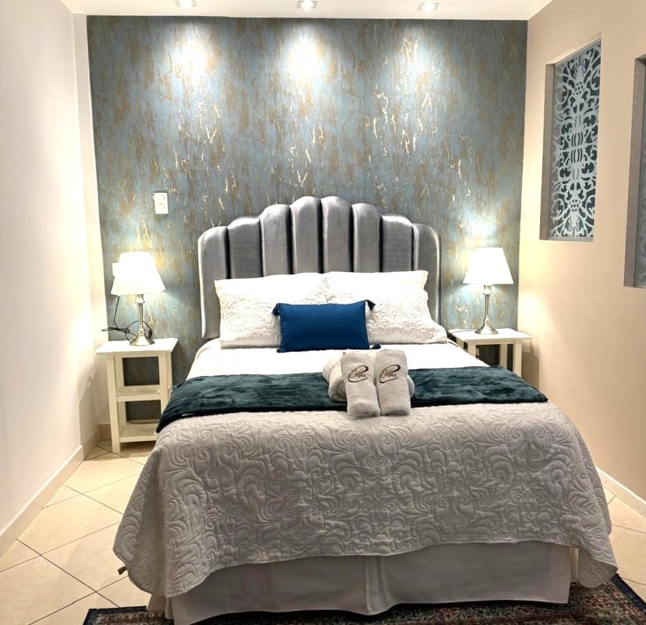 A comfortable sleeping area is highlighted by a plush gray headboard and a soft white quilt draped over a spacious bed. Two bedside tables with lamps provide gentle lighting, while decorative wall accents add subtle character to the room.