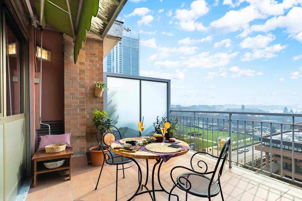 A private terrace is showcased with a round dining table set for two, accompanied by stylish chairs. Potted plants add greenery, while the expansive city views and bright blue sky create a calm outdoor space for relaxation and al fresco dining.