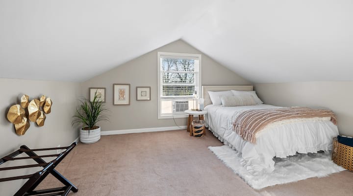 Očarujúci priestor v štýle loftu so šikmými stropmi, mäkkou posteľnou bielizňou a slnečným svetlom prúdiacim cez okno
