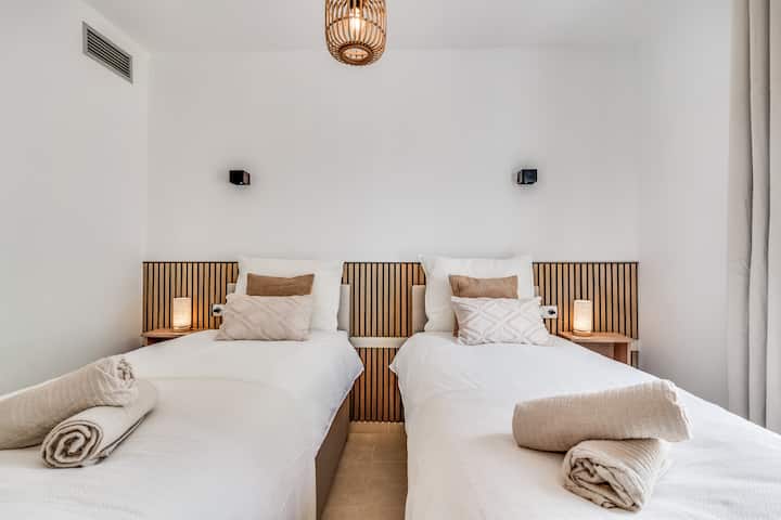 Quarto com duas camas de solteiro, lençóis macios, mesas de cabeceira combinando e iluminação ambiente aconchegante