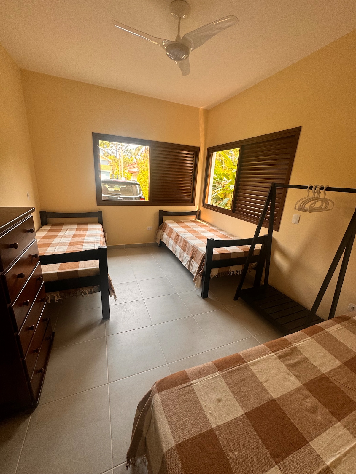 Habitación con 3 camas individuales, ventilador de techo, cómoda y un cajón grande. Está en la planta baja de la casa.