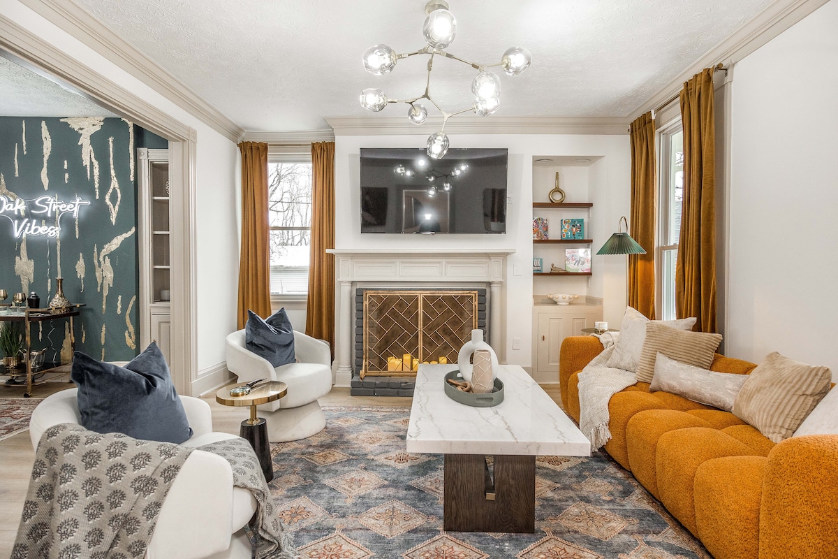 Стилна всекидневна с перфектна комбинация от комфорт и изтънченост. Разполага с мраморна масичка за кафе, диван от горчица, бели акцентни столове и декоративна камина. Съвременното осветление и големите прозорци създават светла, привлекателна атмосфера.