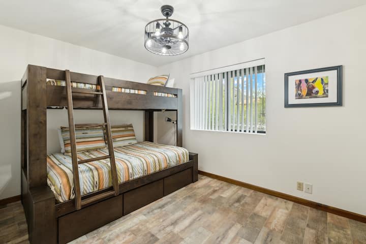 חדר קומותיים בהיר ורב-תכליתי עם מיטת קומותיים יציבה - מושלם לילדים, בני נוער או אפילו מבוגרים - עם מצעים מערביים כיפיים, אורות קריאה מובנים ועיצוב עליז בסגנון מדבר.