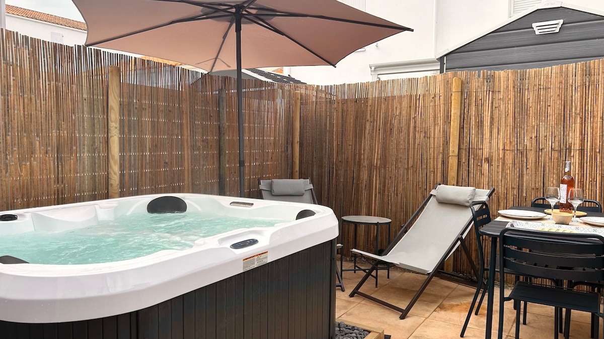 A private terrace is featured, showcasing a spa filled with water, surrounded by bamboo fencing for privacy. Sun loungers and a small table are positioned nearby, complemented by a large umbrella providing shade over the area.