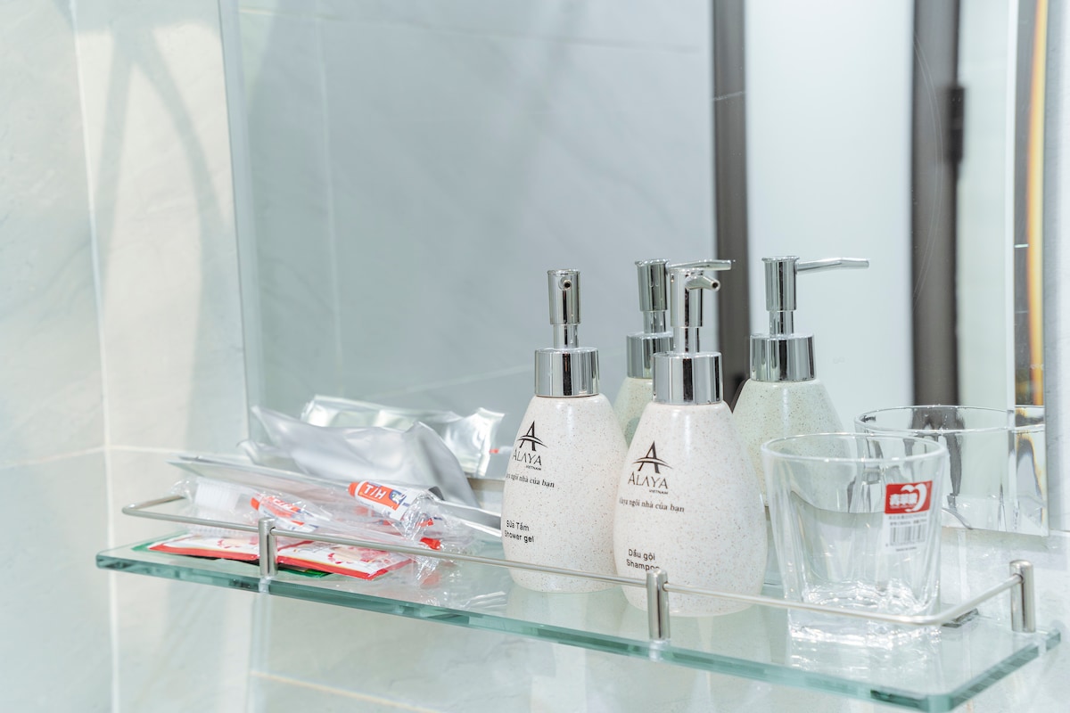 A bathroom shelf is displayed with personal care items. Three elegant dispensers for soap are positioned alongside glass cups. Sachets for toiletries are neatly arranged, providing essential amenities for guests.
