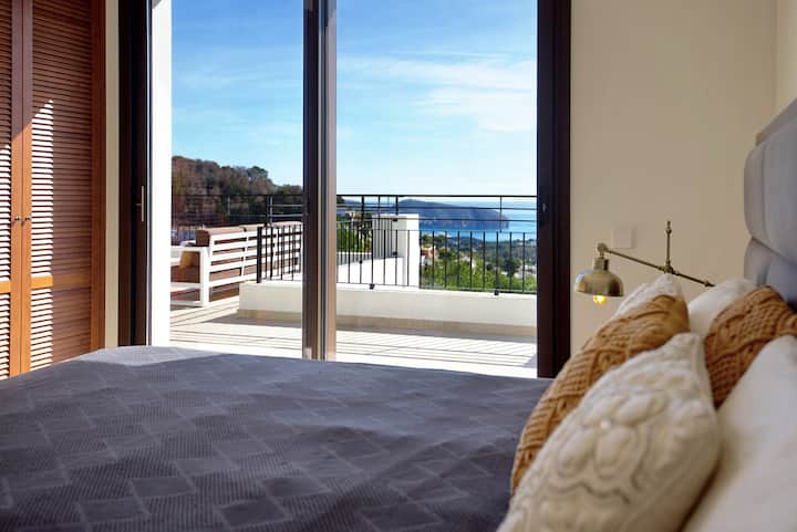 Priestranná, elegantná spálňa s úchvatným výhľadom na more cez sklenené dvere od podlahy až po strop, ktoré sa otvárajú na veľkú terasu. Izba je kúpaná v prirodzenom svetle a vytvára pokojnú a vzdušnú atmosféru.