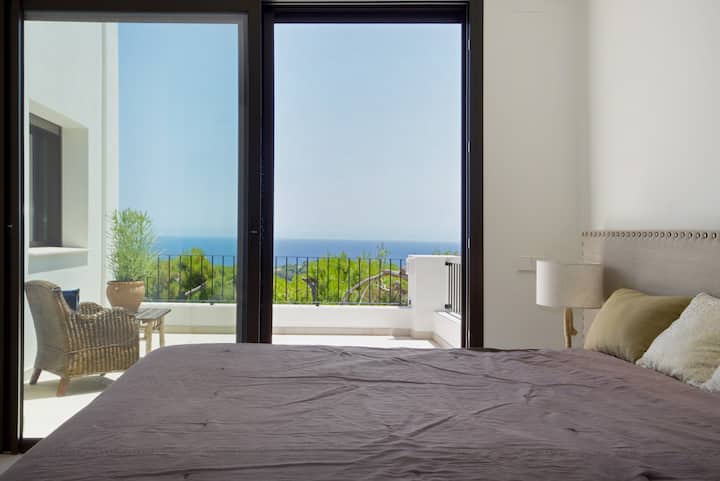 Priestranná, elegantná spálňa s úchvatným výhľadom na more cez sklenené dvere od podlahy až po strop, ktoré sa otvárajú na súkromnú terasu. Izba je kúpaná v prirodzenom svetle a vytvára pokojnú a vzdušnú atmosféru.