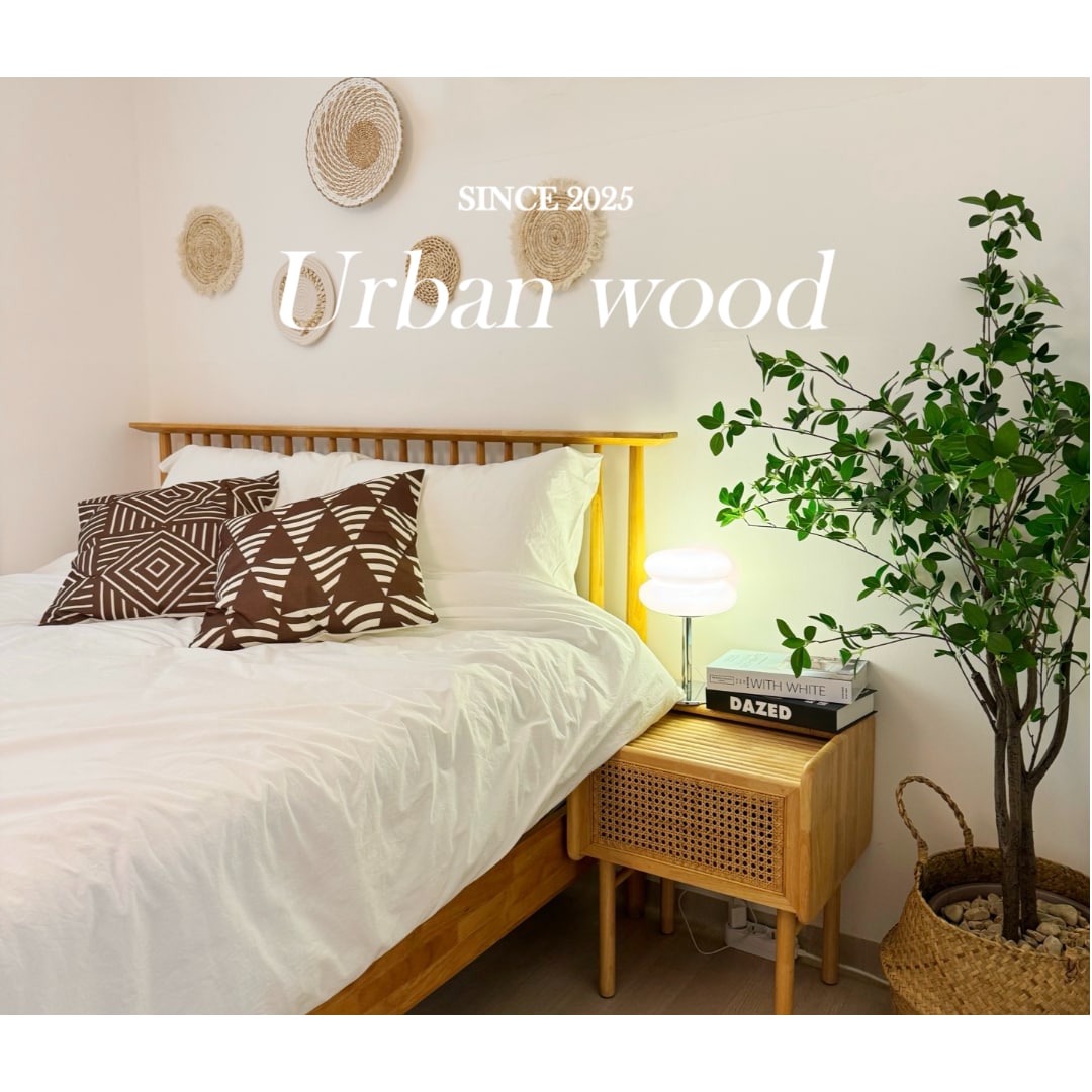 A cozy bedroom includes a spacious bed adorned with patterned pillows and crisp white linens. A bedside table features a stylish lamp and a small decorative plant. Woven wall decor adds texture to the room, enhancing its natural aesthetic.
