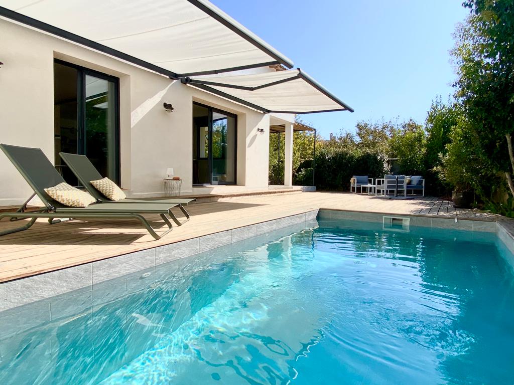 A refreshing private pool is surrounded by a wooden deck and lounge chairs, providing a perfect spot for relaxation. Nearby, shaded areas created by awnings offer comfort. The garden area showcases greenery, enhancing the tranquil outdoor setting.