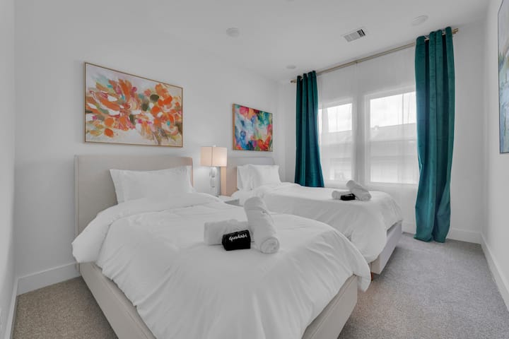 Სტუმრების კომფორტული საძინებელი ორადგილიანი საწოლით, ფერადი ხელოვნების ნიმუშებითა და უშუქო ფარდებით