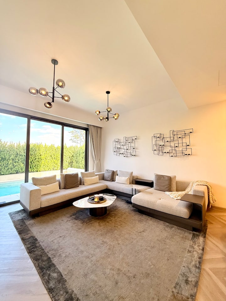 Опуштете се удобно со овој голем кауч во форма на буквата L, со меки перници, две вградени конзоли, масичка за кафе и масичка за кауч. Уживајте во пијалаци или работете на вашиот лаптоп додека го гледате надворешниот базен со стил и удобност.