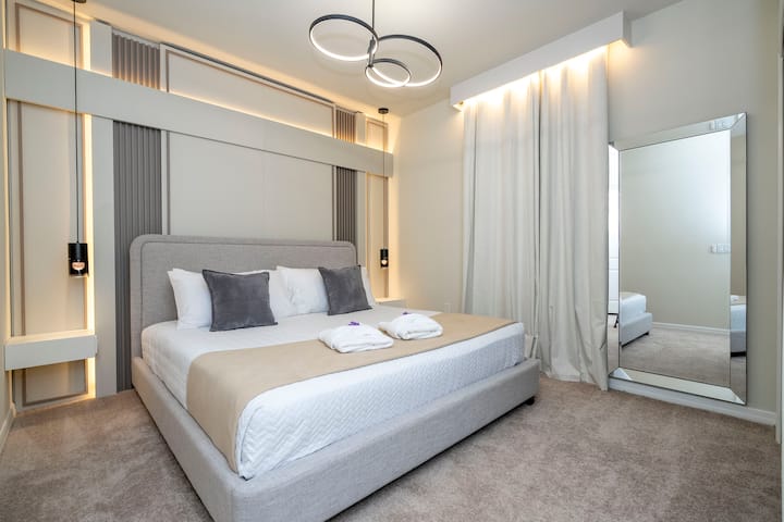 غرفة نوم مفروشة في الطابق السفلي مع سرير كينج ووسائد ناعمة وتلفزيون وخزانة مع ستائر تعتيم