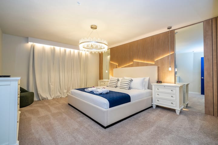 غرفة نوم رئيسية في الطابق العلوي مع حمام كامل ملحق وخزانة ملابس وخزانة ودولاب أمان وتلفزيون وساعة منبه مع ستائر تعتيم. 