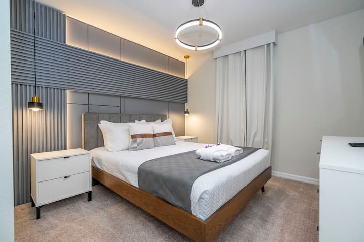 غرفة نوم مفروشة في الطابق العلوي مع سرير متوسط الحجم ووسائد ناعمة وتلفزيون وخزانة مع ستائر تعتيم وحمام كامل ملحق