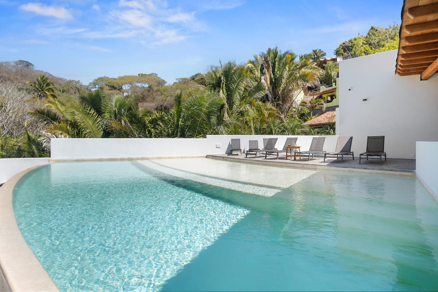 Shared rooftop infinity pool with sun loungers and forest views