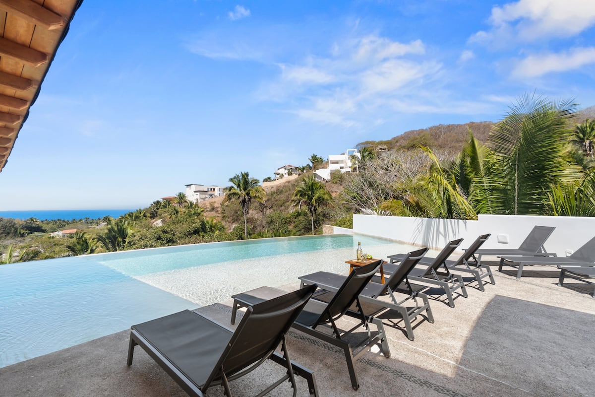 Infinity pool edge and sun loungers looking toward the ocean