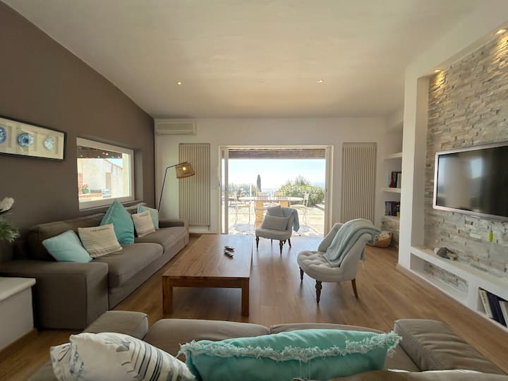 dhoma e ndenjjes e bollshme dhe e ndritshme që hapet në një tarracë me pishinë dhe pamje nga deti