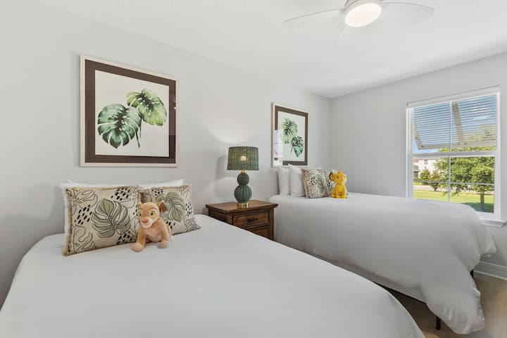 Relax in this Lion King-themed bedroom featuring two full-sized beds with crisp white linens, a smart TV, full dresser, and closet for storage. The clean, simple bedding lets the vibrant decor and safari adventure shine!