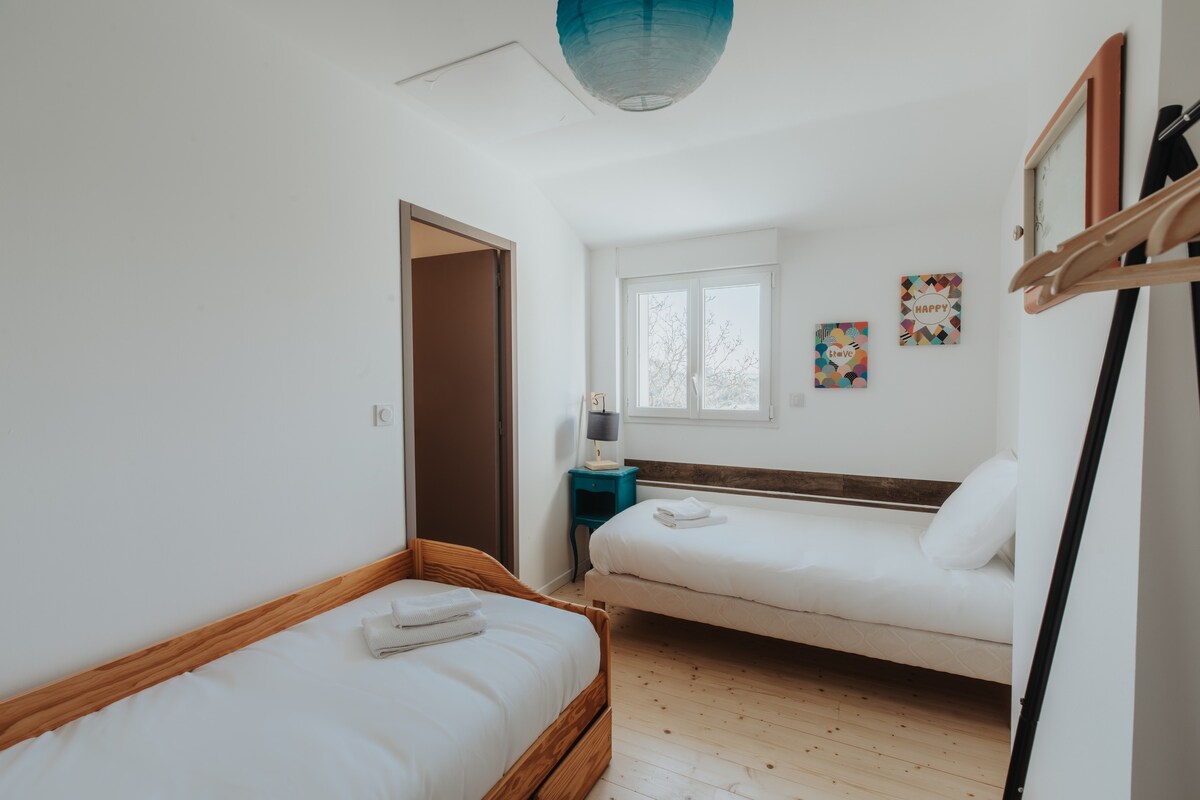 חדר שינה מואר עם שתי מיטות יחיד, מצעים ומגבות.