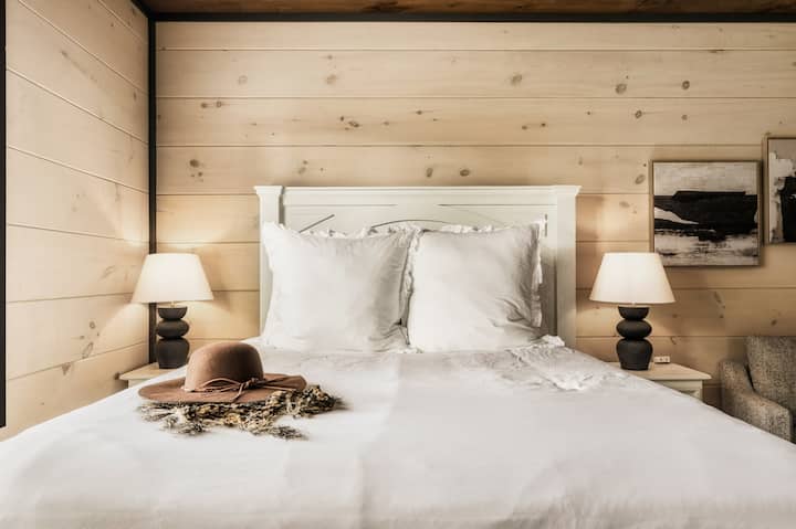 Kitanda chenye starehe na mito ya kupendeza, taa za kitanda zenye joto na kuta za mbao.