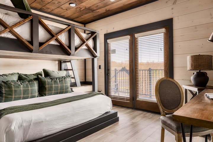 Chumba cha ghorofa cha kijijini kilicho na kitanda chenye starehe, madirisha makubwa na mihimili ya mbao.