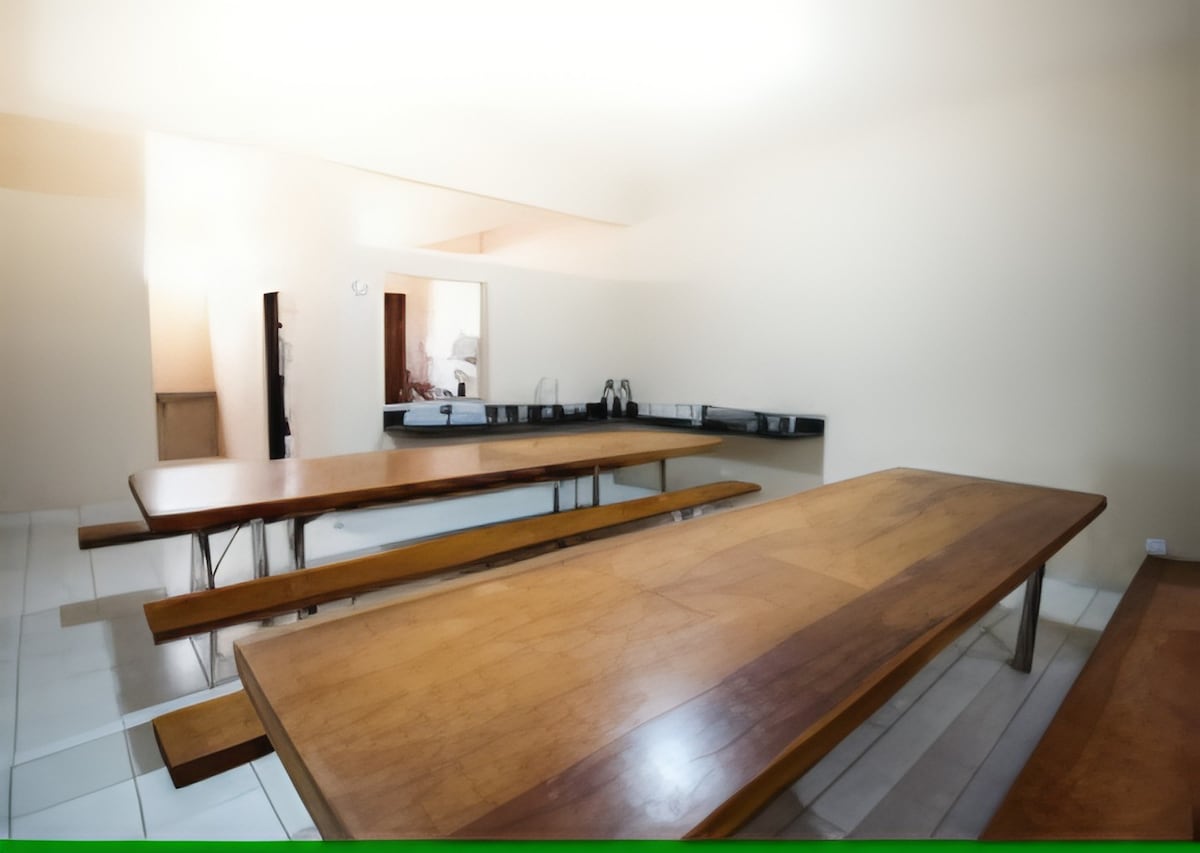 The dining area features several long wooden tables designed for communal meals. The space is equipped with a counter area and includes kitchen essentials. Neutral-colored walls and ample lighting create a spacious environment for guests to gather.