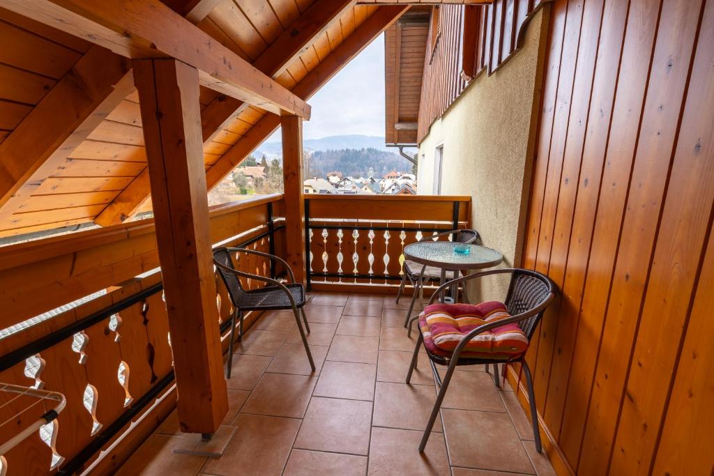 A wooden balcony features two chairs and a small table, providing a cozy outdoor space. The balcony is adorned with traditional wooden railings, and views of the surrounding landscape can be seen in the distance.