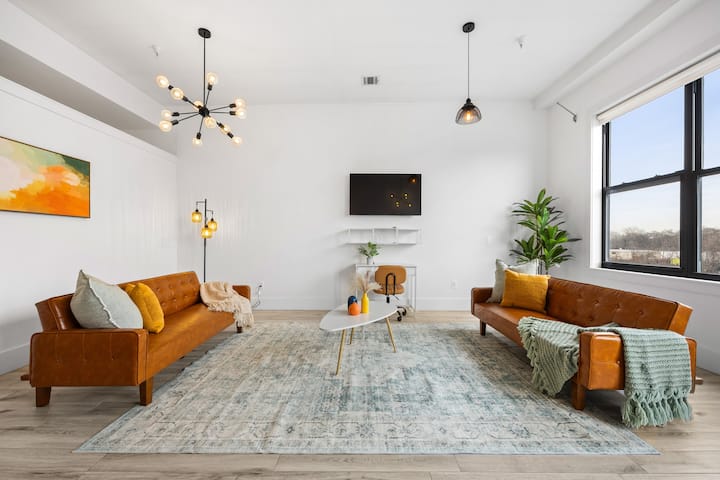 Espaço de estar luminoso e convidativo, com decoração moderna, tetos altos e janelas grandes.