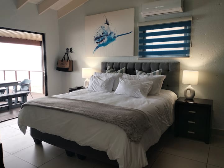 Ampia camera da letto matrimoniale con letto soffice, luci soffuse e accesso diretto alla terrazza privata per godere di una tranquilla vista sull'oceano al mattino.