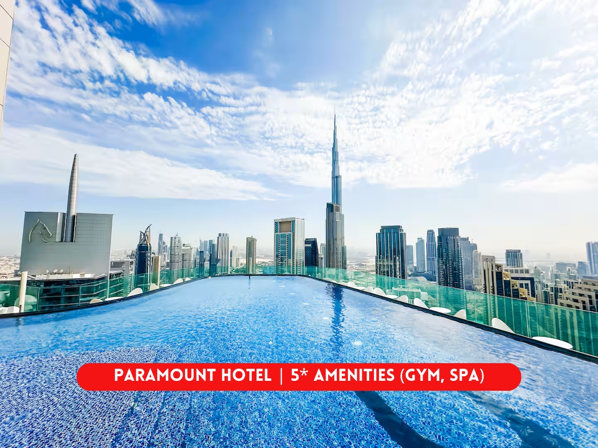A rooftop infinity pool shimmers under the bright sky, offering panoramic views of the Burj Khalifa and the surrounding skyline. The pool's vibrant blue water contrasts with the sleek glass buildings, creating an inviting atmosphere for relaxation and enjoyment.