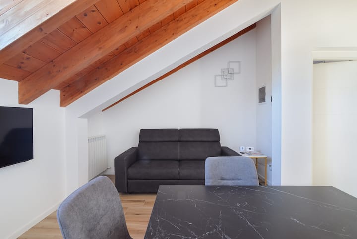 Дневната соба се отвора под покрив со изложени дрвени греди, што веднаш ја прави околината топла и пријатна. Добро распоредени: од една страна елегантна трпезариска маса со тапацирани столови, од друга страна удобен кауч на спуштање и телевизор со Netflix.