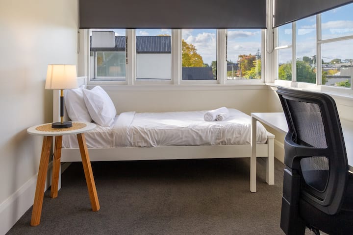 Krevet za jednu osobu s čistom posteljinom, radni prostor s ergonomskom uredskom stolicom