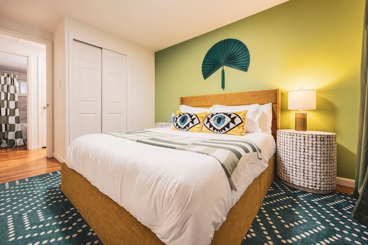 غرفة نوم مريحة مع سرير بحجم كوين، وجدار أخضر عصري، ووسائد جريئة، وأغطية سرير ناعمة، وديكور أنيق. تتميز بمصباح بجانب السرير وسجادة منقوشة ومساحة خزانة - مثالية لقضاء ليلة مريحة.