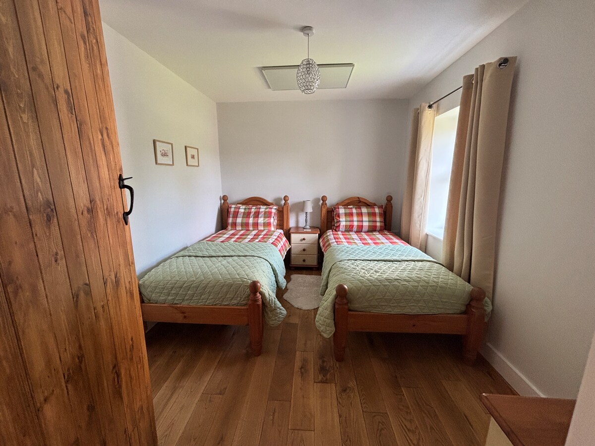 Chumba cha kulala kilicho mbele ya nyumba chenye vitanda viwili vya mtu mmoja, makabati, kifua cha droo na hanger ya nguo