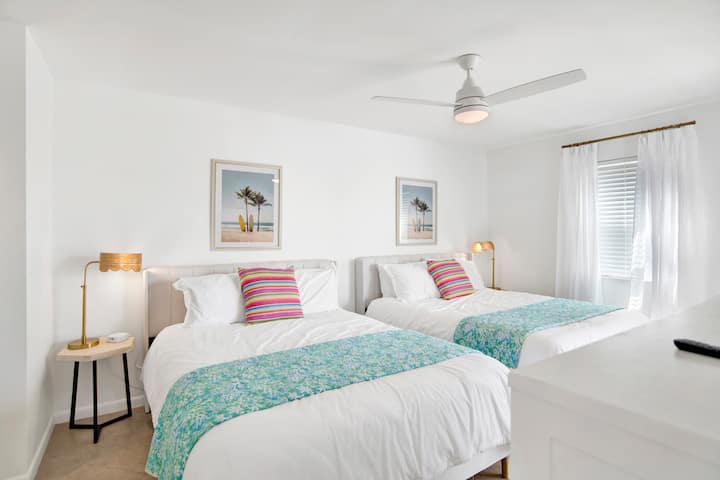 غرفة نوم كبيرة بسريرين بحجم كوين وطاولات جانبية مع مصابيح وقابس لعدة أجهزة