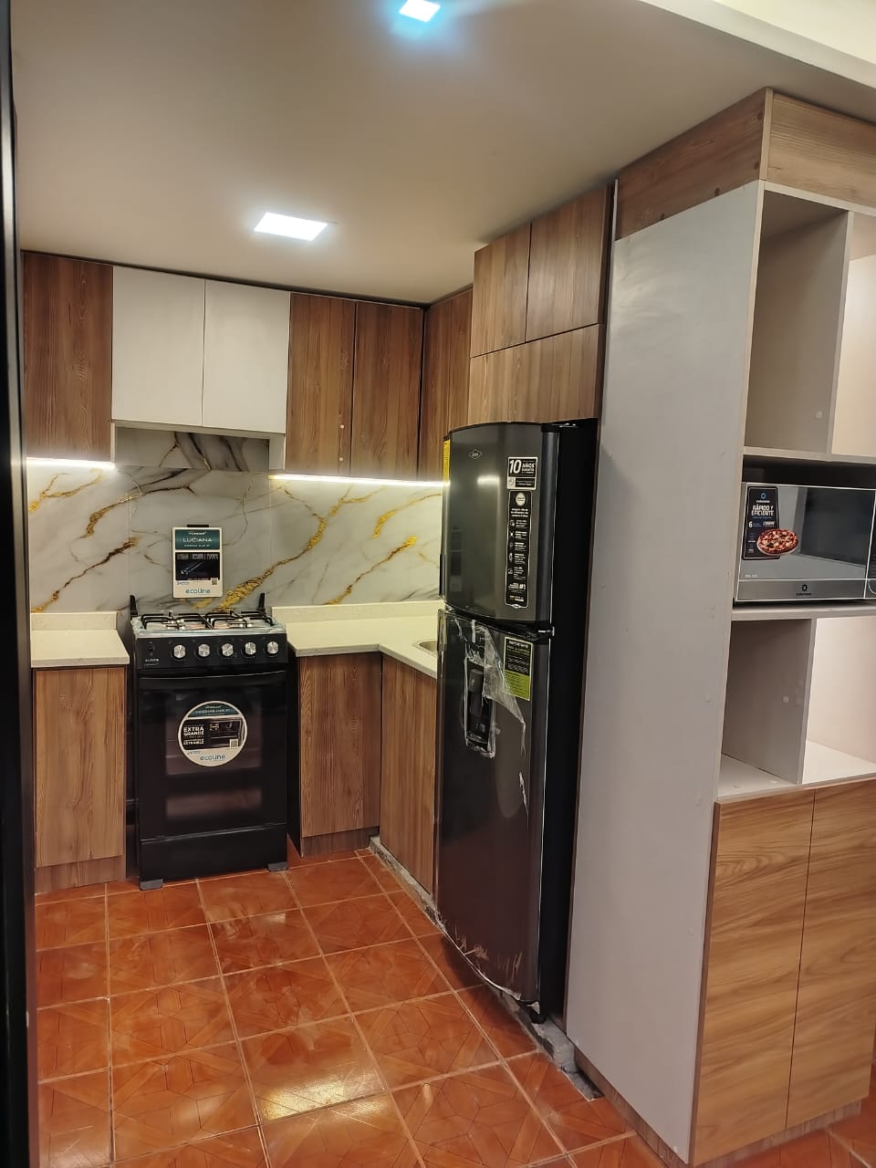 A modern kitchen features wooden cabinetry with a marble backsplash. Essential appliances include a stove, a refrigerator, and a microwave. Ample counter space is present for meal preparation, with warm lighting enhancing the practical layout.