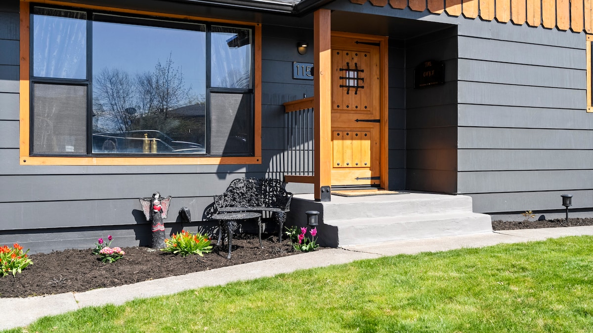 The exterior of the home features a welcoming entrance with a wooden door and decorative grillwork. A black bench is positioned on a stone path, complemented by vibrant flower beds and a well-manicured lawn, enhancing the inviting appearance of the property.