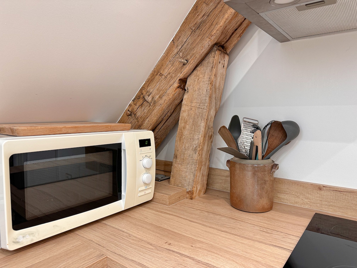 The kitchen area features exposed wooden beams paired with a modern countertop. A microwave and a container filled with cooking utensils are set on the surfaces, offering essential tools for meal preparation. The warm tones of wood contribute to the overall welcoming atmosphere.